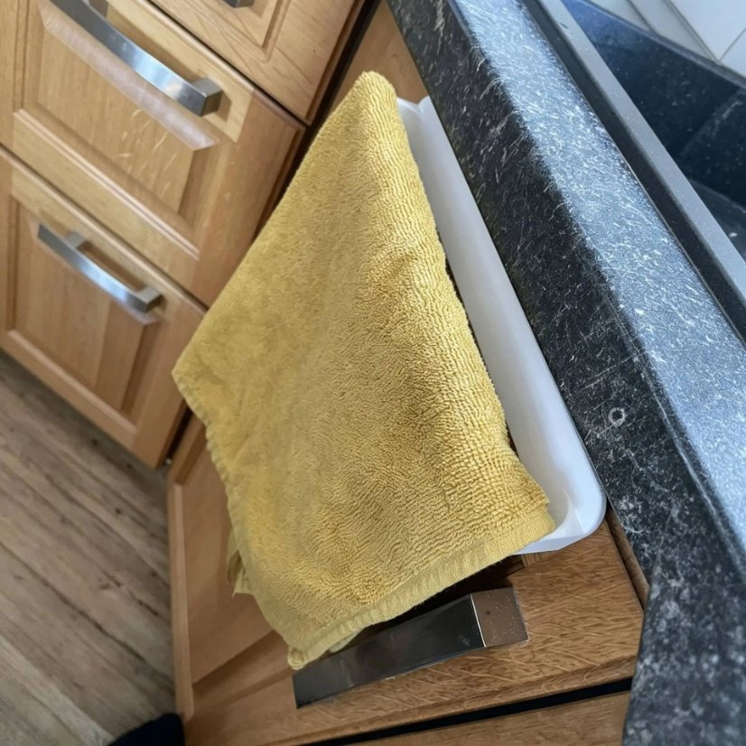 White cabinet towel rack shown with a yellow towel beside a wooden cabinet door.